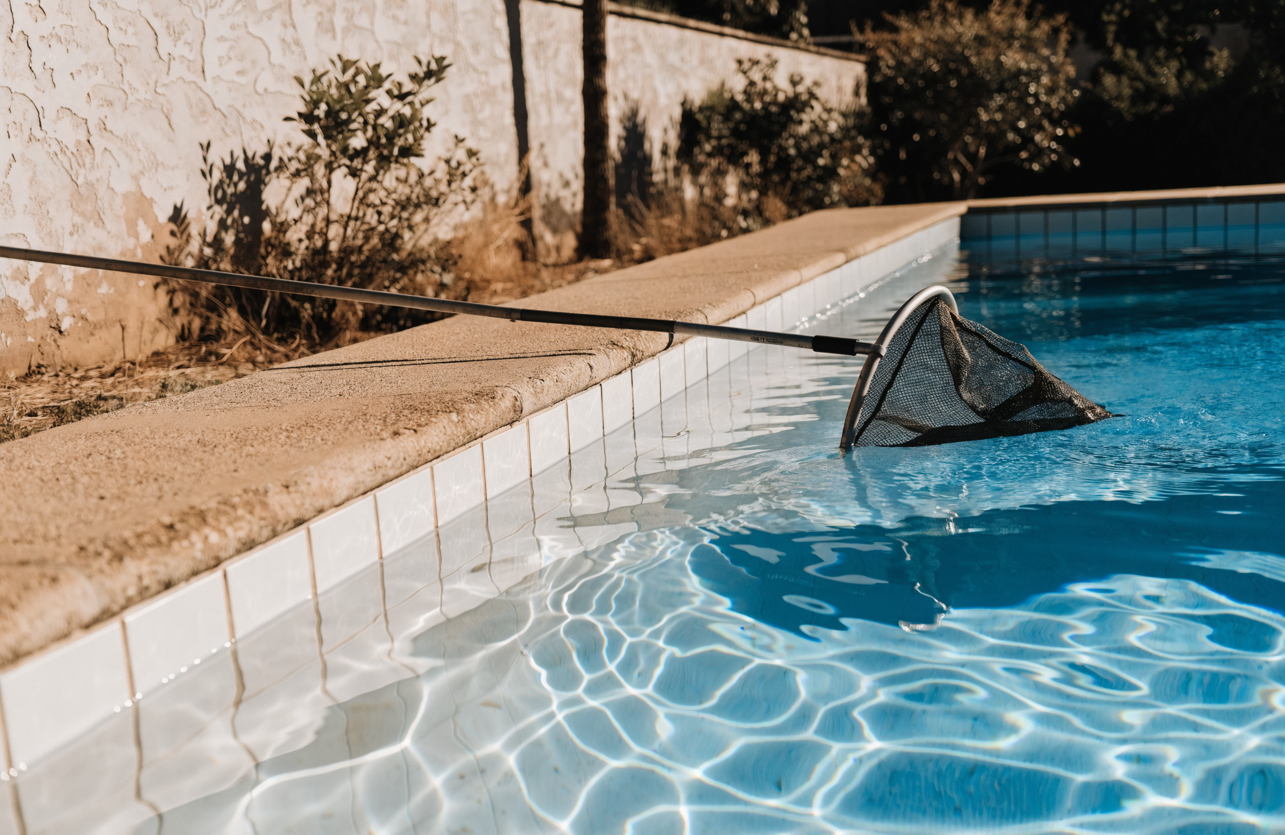 Skimmer net resting on the edge of a clear blue backyard swimming pool